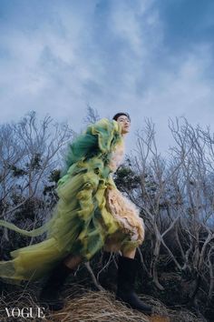 a woman in a green and yellow dress standing on top of a dry grass field