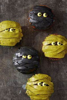 four decorated cupcakes with yellow eyes and black icing on a gray surface