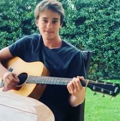 a young man sitting in a chair holding an acoustic guitar