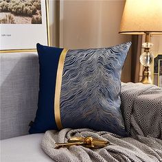 a close up of a pillow on a bed with a blanket and lamp in the background