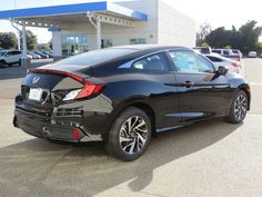 the rear end of a black car parked in front of a gas station with other cars