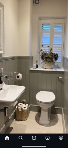 a white toilet sitting next to a sink in a bathroom under a window with shutters