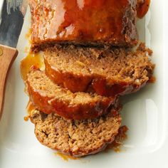 sliced meatloaf sitting on top of a white plate next to a knife