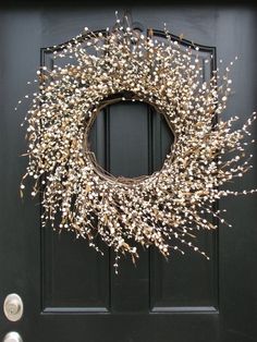 a black door with a wreath on it and white flowers hanging from the front window