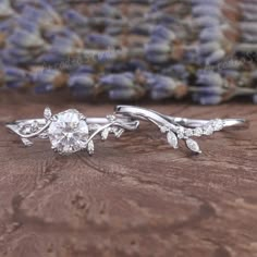 two wedding rings with leaves and diamonds on them sitting on a table next to lavender flowers