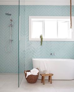 a white bath tub sitting under a window next to a wooden stool in a bathroom