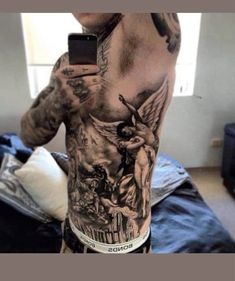 a man with tattoos on his back holding a cell phone and taking a selfie