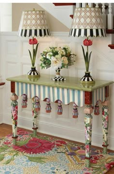 a table with two lamps on top of it next to a rug and some flowers