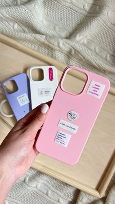 a hand holding a pink and blue phone case on top of a wooden tray next to a white cell phone