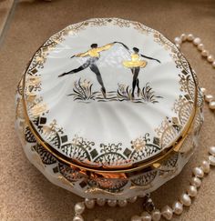 a white and gold box with two ballerinas painted on the front, surrounded by pearls