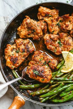 chicken and asparagus in a skillet with lemon wedges