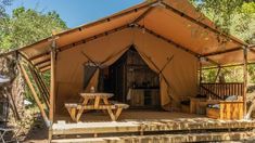 a large tent set up in the woods with picnic tables and chairs around it for people to eat