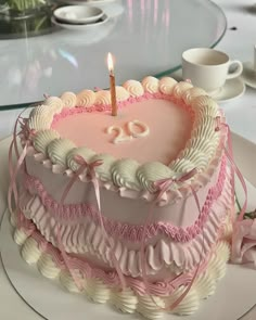 a pink and white birthday cake with a candle on it's top, sitting on a plate