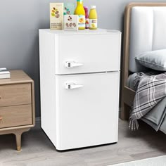 a white refrigerator freezer sitting next to a night stand with bottles on top of it