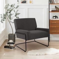 a gray chair sitting next to a book shelf and a potted plant on top of a hard wood floor