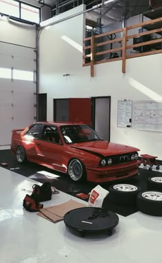 a red car parked in a garage next to some tires and other items on the floor