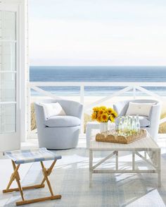 a living room with white furniture and sunflowers on the table in front of the ocean