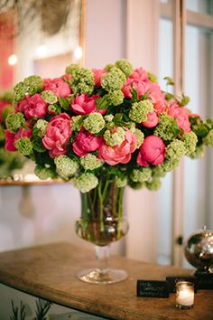 a vase filled with pink and green flowers on top of a table next to a mirror