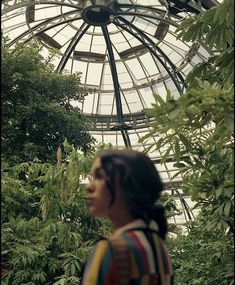 a woman standing in front of a glass dome with trees around her and bushes behind her