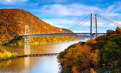 a large bridge spanning over a river surrounded by trees with fall foliage on the hillside