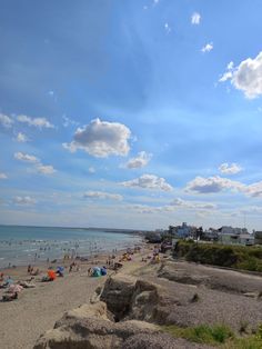 many people are on the beach and in the water at this time, there is a blue sky with white clouds