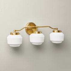 three light bathroom fixture in brass finish with white glass shades on the arms and sides