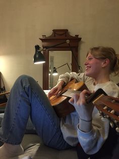 a woman sitting on top of a bed holding an acoustic guitar in her hands and smiling