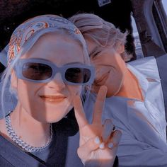 two women in sunglasses making the v sign with their fingers while sitting next to each other