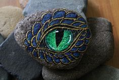 a rock with an eye painted on it sitting next to some rocks and stones in the shape of peacock feathers