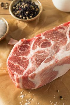 raw meat sitting on top of a wooden table next to spices and pepper shakers