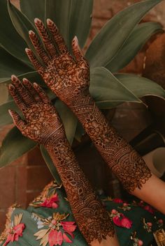 two hands with henna tattoos on their palms and palm leaves in the foreground