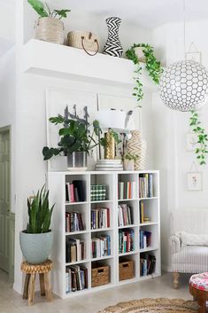 a living room with bookshelves and plants on the top shelf, in front of a white wall