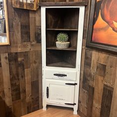 a white cabinet sitting in the corner of a room with wood paneling on the walls