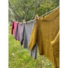 several sweaters hanging on a clothes line in front of green grass and trees,