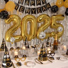 a table topped with lots of balloons and black and gold decorations for a new year's eve party