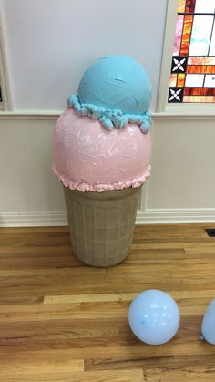 an ice cream cone with pink and blue frosting on top, next to balloons