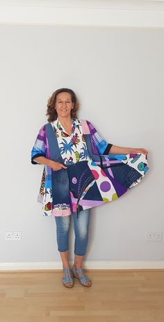 a woman standing in front of a white wall holding onto a colorful piece of cloth