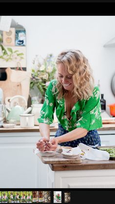 a woman in a green shirt is preparing food on a wooden table with white cabinets