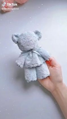 a hand holding a small gray teddy bear