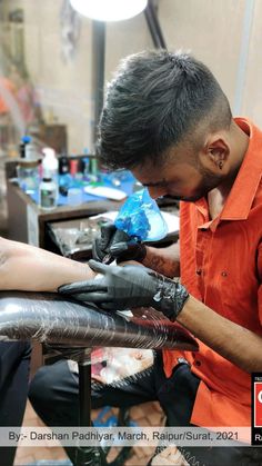 a man in an orange shirt and black gloves is doing something on another mans arm