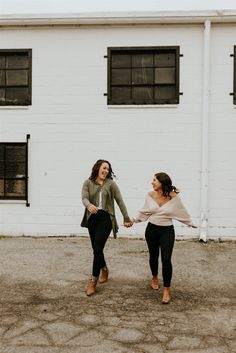 two women holding hands in front of a white building