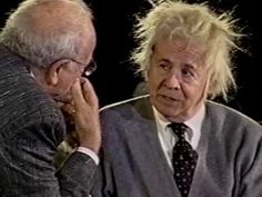 an old man with white hair and glasses talking to another older man who is wearing a suit