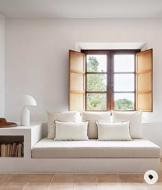 a white couch sitting under a window next to a book shelf