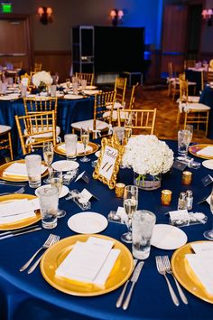 the table is set for an event with blue linens and gold chargers