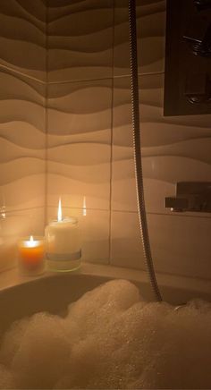 two candles sitting in the middle of a bathtub filled with foam and bubbles next to a shower head