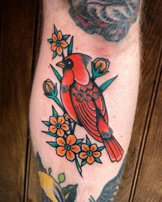 a red bird sitting on top of a branch with flowers and leaves around its neck