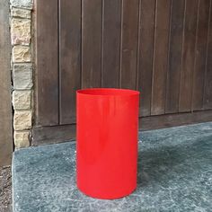 a red vase sitting on top of a cement slab next to a wooden wall and door