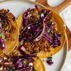 three tacos on a plate topped with shredded cabbage and other toppings next to a fork