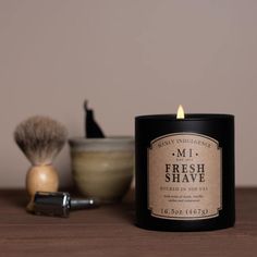 a black candle sitting on top of a wooden table next to a shaving brush