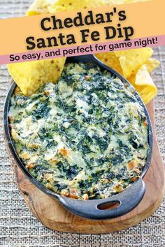 a bowl filled with spinach dip next to tortilla chips on a table